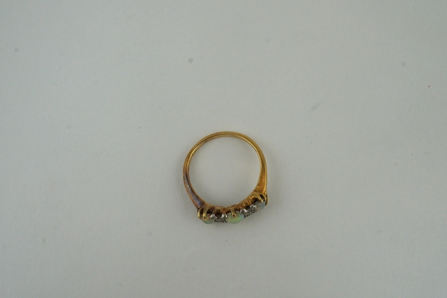 A yellow metal (stamped 18) and three stone white opal set half hoop ring, with diamond chip spacers, size M, gross weight 3.1 grams. Condition - poor to fair